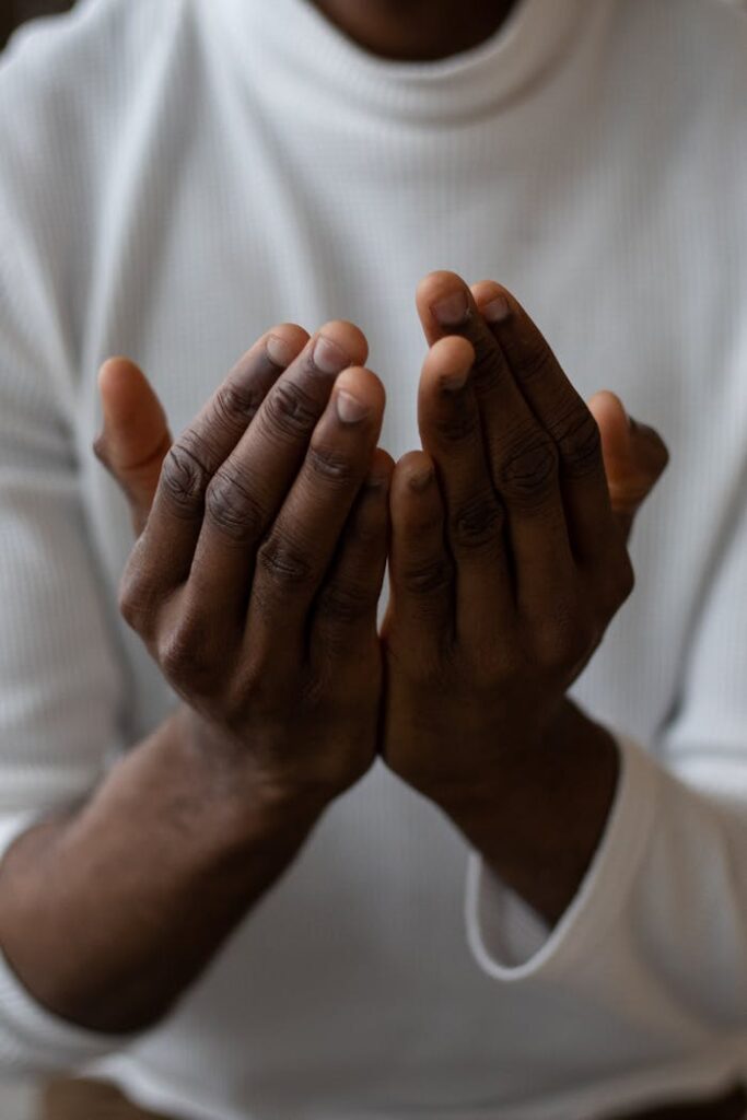 Selective focus of crop anonymous African American man wearing white turtleneck praying with open hands